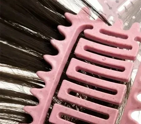 Mèche de cheveux bouclés mouillés tenue à deux mains, la brosse passée sur les pointes puis remontée vers la racine.